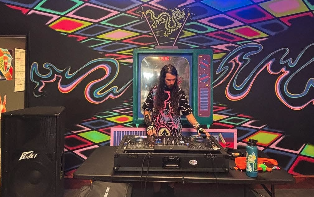 DJ spinning in front of the neon dragon mural at the shop